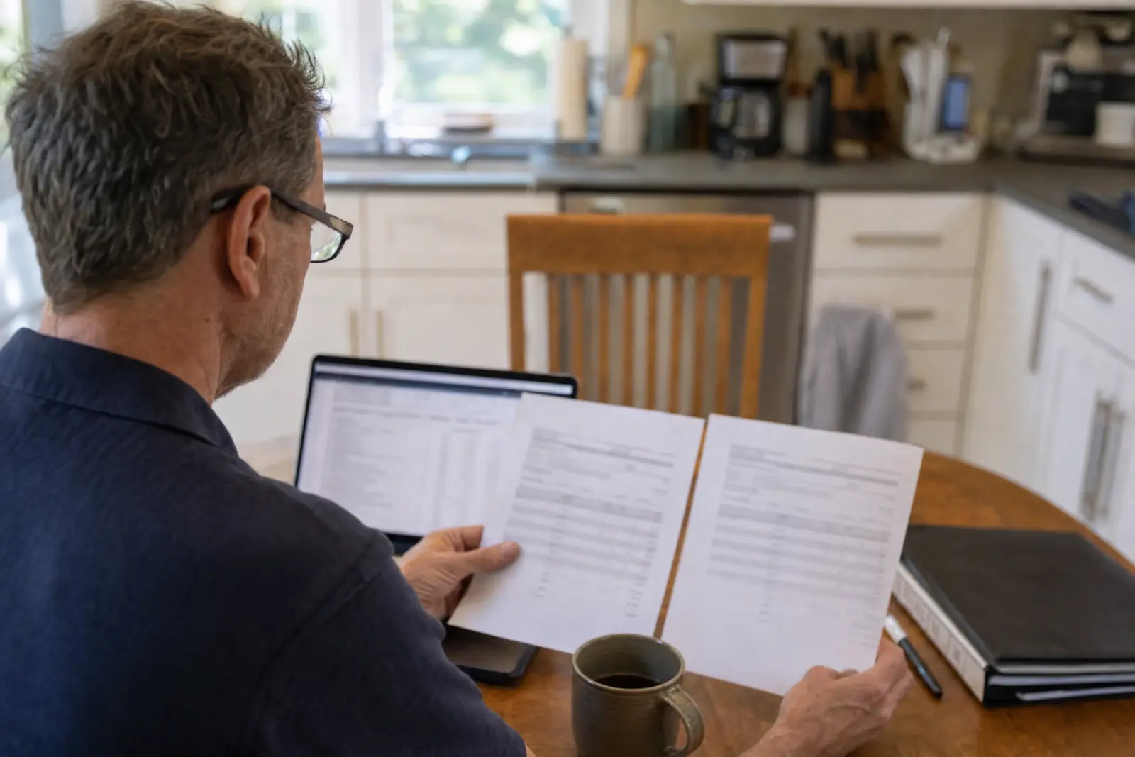 A homeowner comparing two printed estimates at his kitchen table