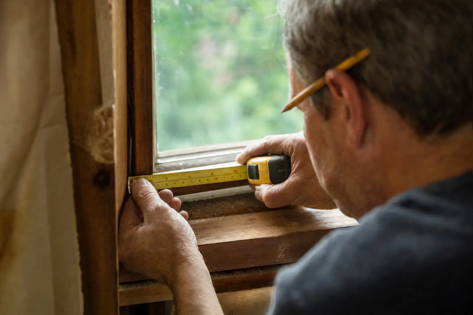 A contractor measuring a window frame with a tape measure